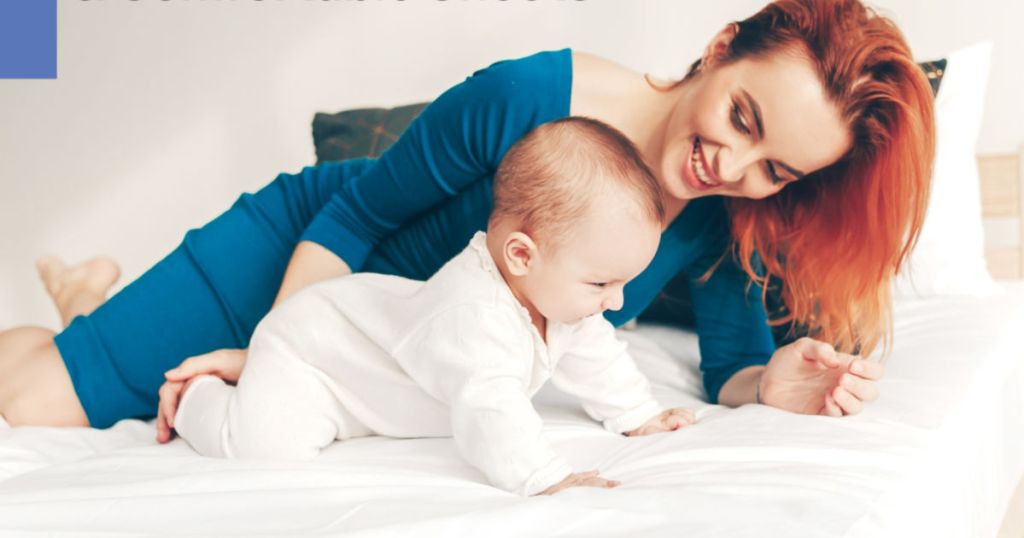 mom and baby laying on a bed with white sheets