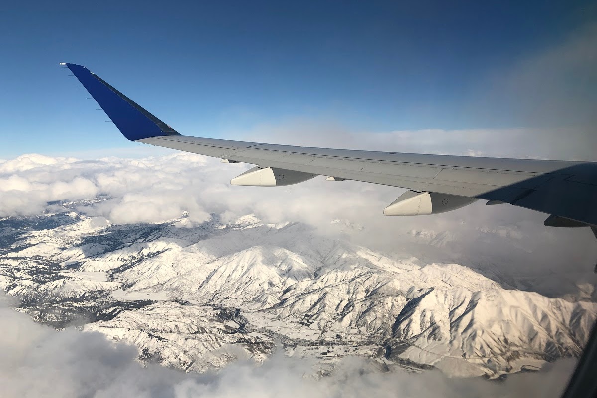 airplane wing over snowy mountains vacation on a budget