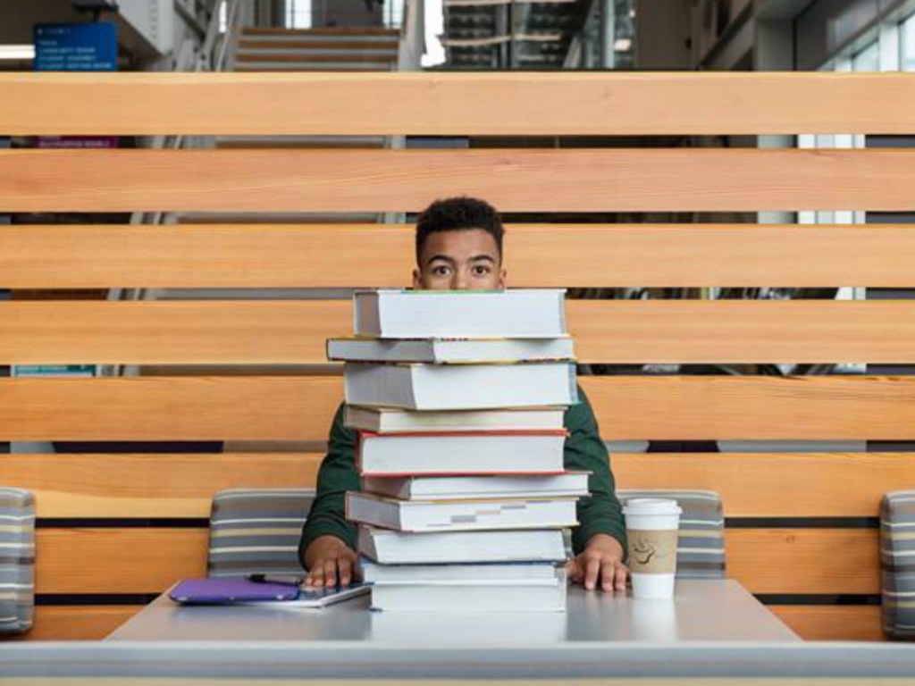college student with stack of text books at table
