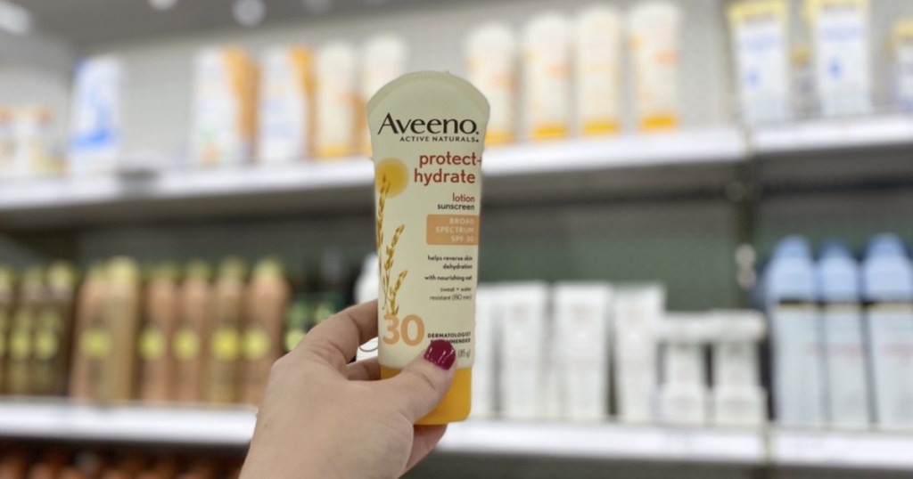hand holding aveeno sunscreen in store with bottles behind it