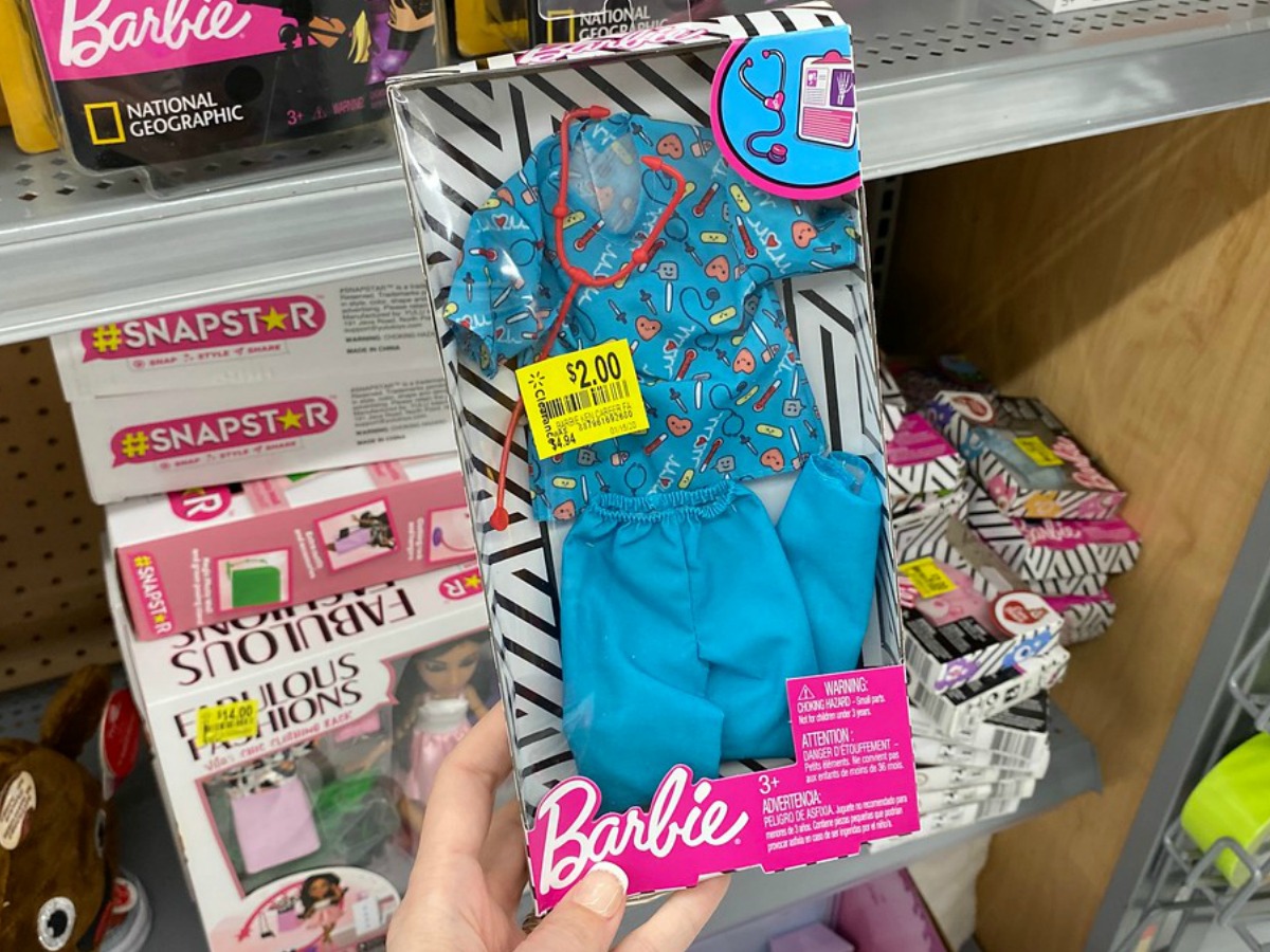 hand holding package with clothes for a doll in front of store display