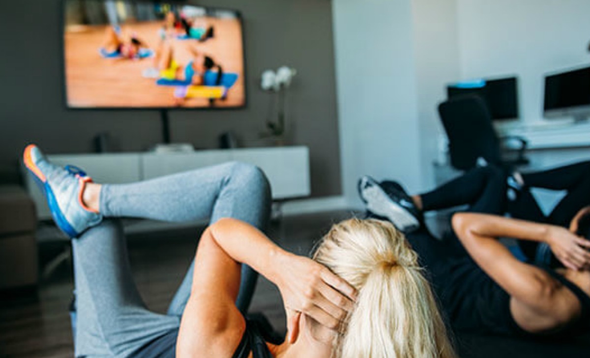 women on floor exercising following workout program on the tv