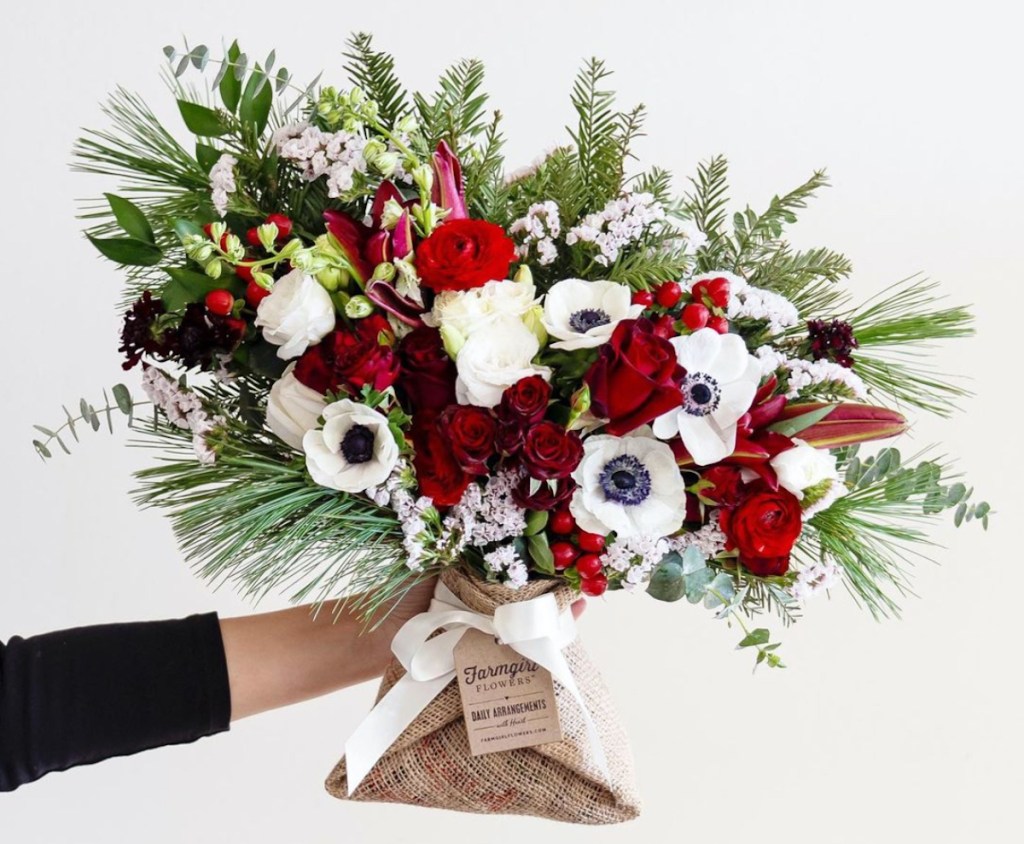 hand holding a bouquet of red and white flowers with greens wrapped in burlap