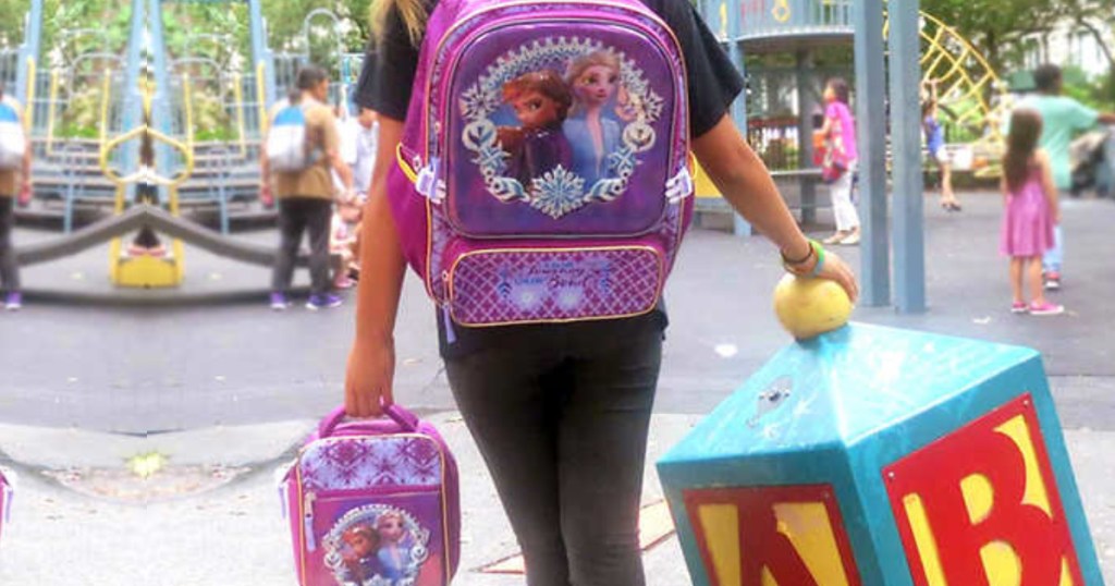 girl walking with backpack on and carrying lunch bag