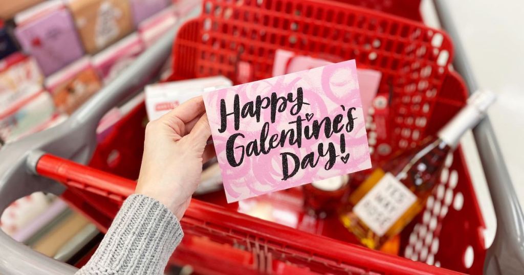 hand holding pink happy galentines day card with red cart behind it