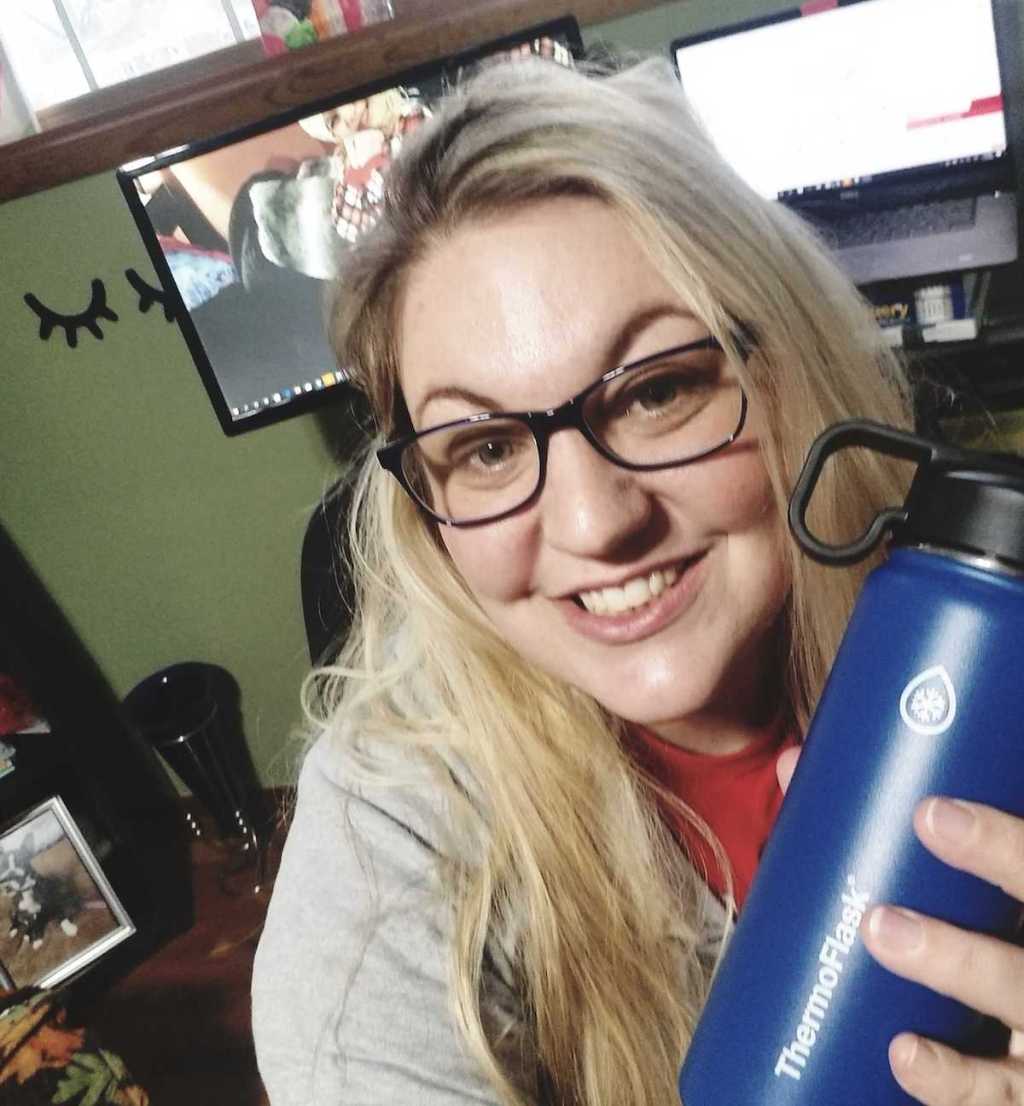 woman wearing glasses smiling holding blue reusable water bottle