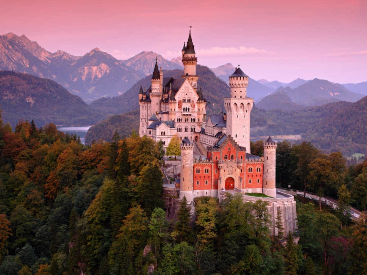 castle near the mountains and trees with pink sunset