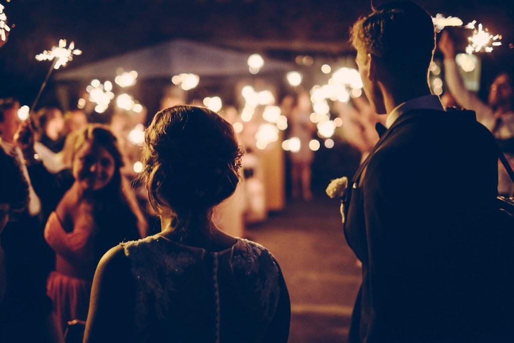 couple bride and groom standing with guests in dark with sparklers