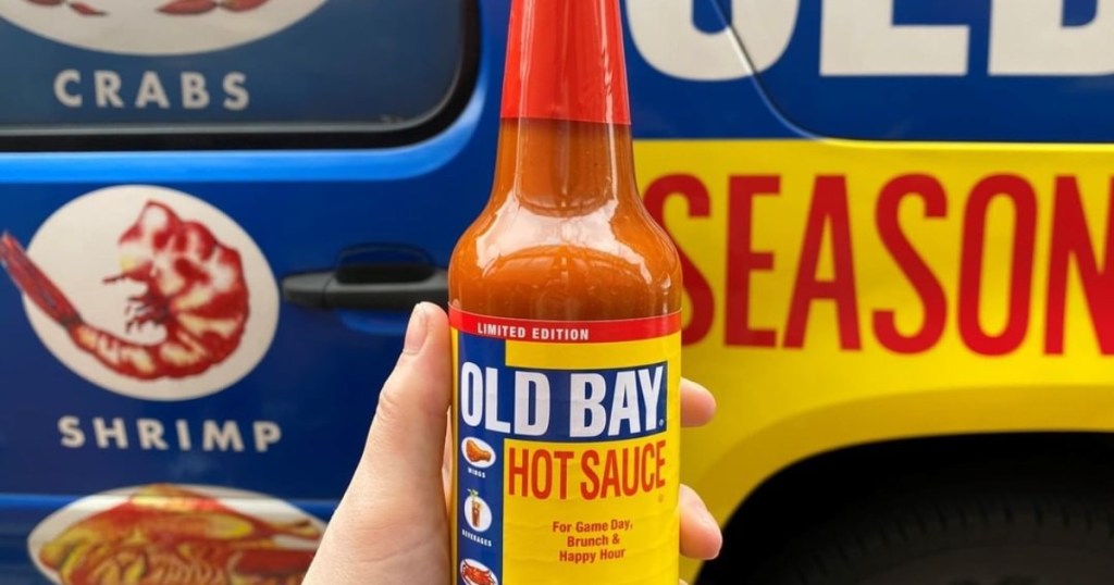 hand holding Old Bay hot sauce in front of Old Bay truck