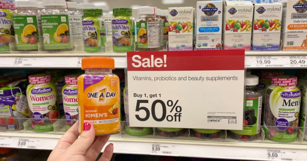 woman holding one a day women's vitamins in front of buy 1 get 1 50% off sale