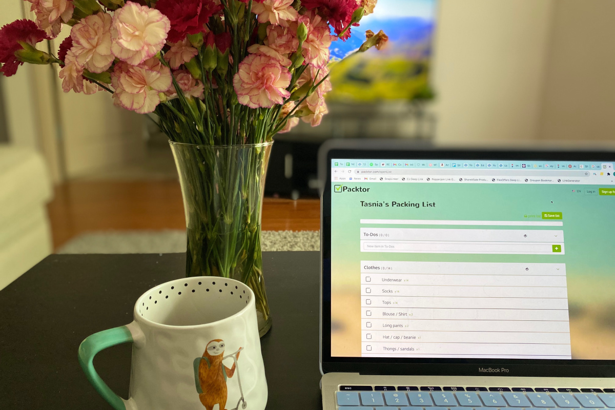 coffee mug and flower vase beside laptop with packing list to score travel deals