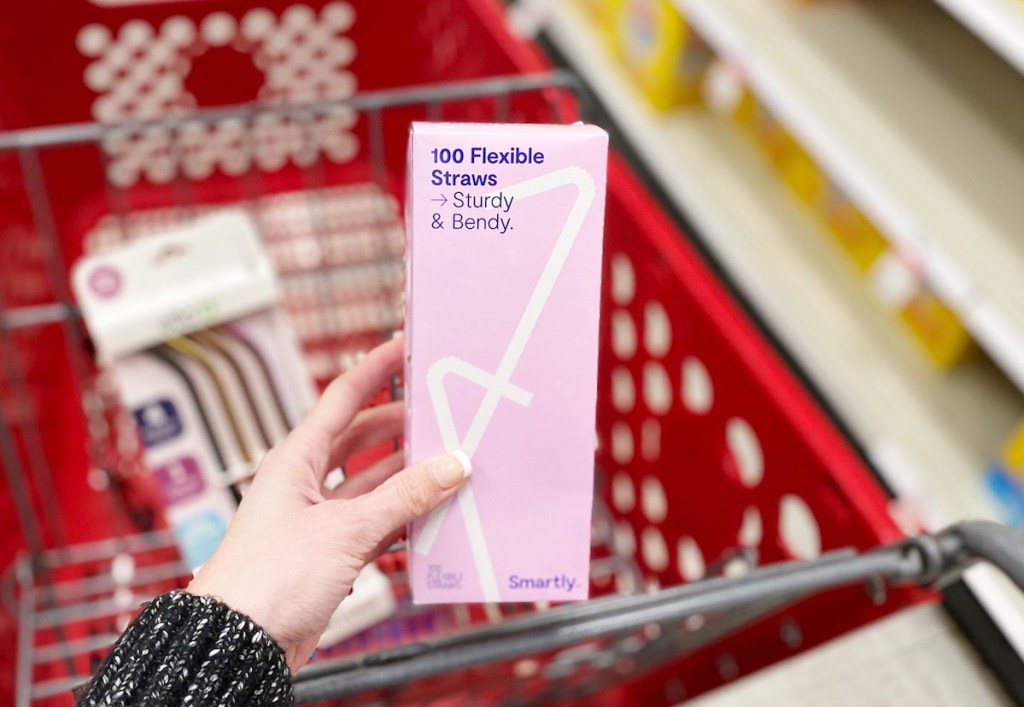 hand holding waste of money pink plastic straws with target cart in background