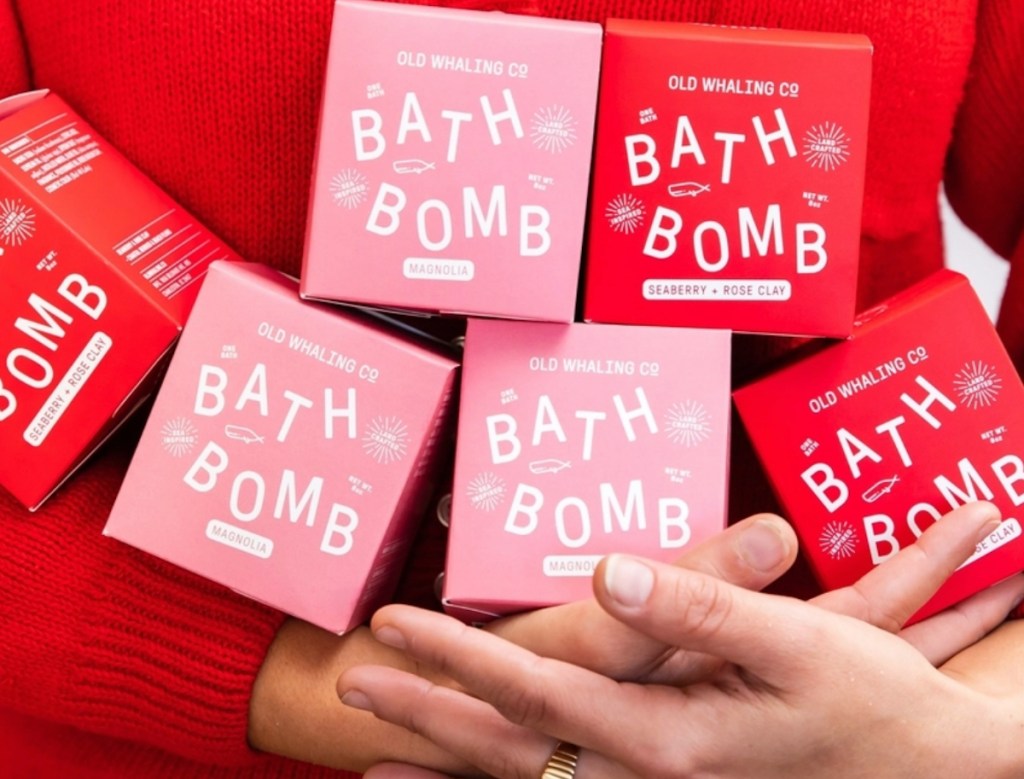 woman wearing bright red sweater with pink and red boxed bath bombs in arms