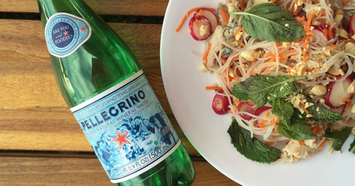 s. pellegrino bottled water next to a plate of rice noodles and vegetables