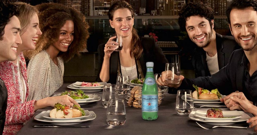 men and women around a table of food with mineral water bottle featured in the center