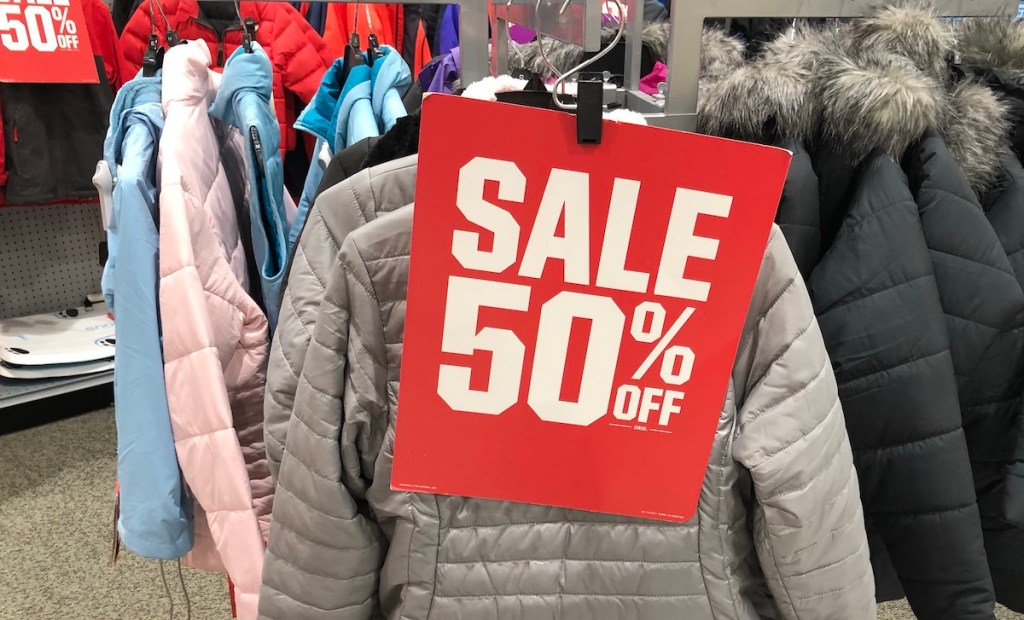 red and white sale 50% off sign hanging on rack of winter coats
