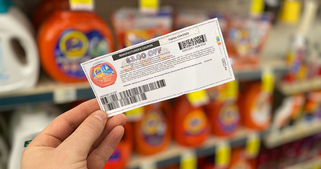 Hand holding a tide coupon in front of a shelf of tide