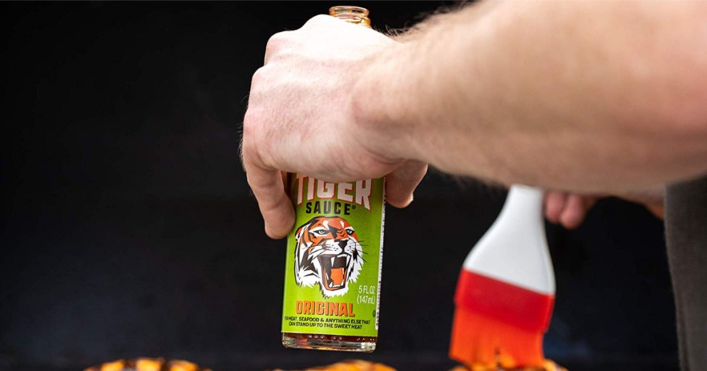 hand holding tiger sauce bottle in one hand and brushing meat with the other hand