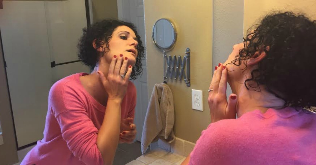 woman holding hand to her face looking in mirror