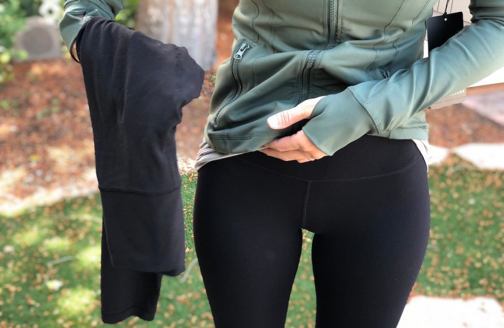 woman wearing black leggings holding up another pair next to her outside
