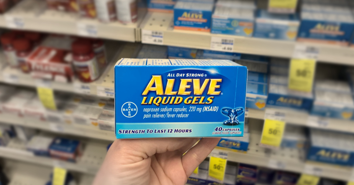 Hand holding Aleve in front of shelf 