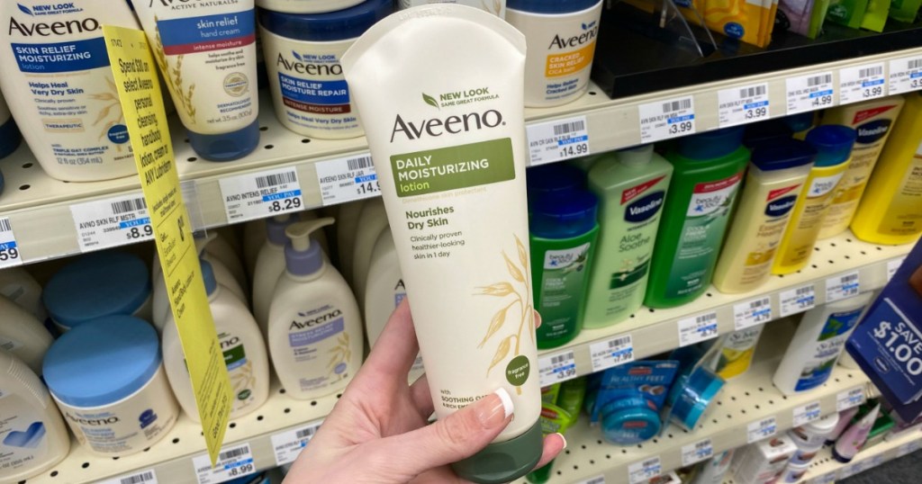 Woman's hand holding a tube of body lotion in front of in-store display