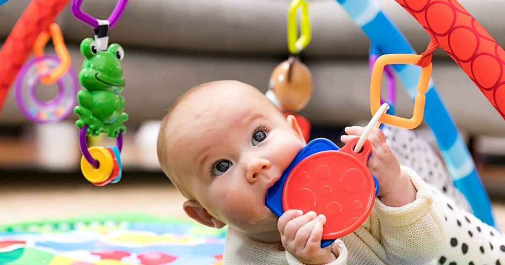 baby on the floor playing with hanging toys from a playmat
