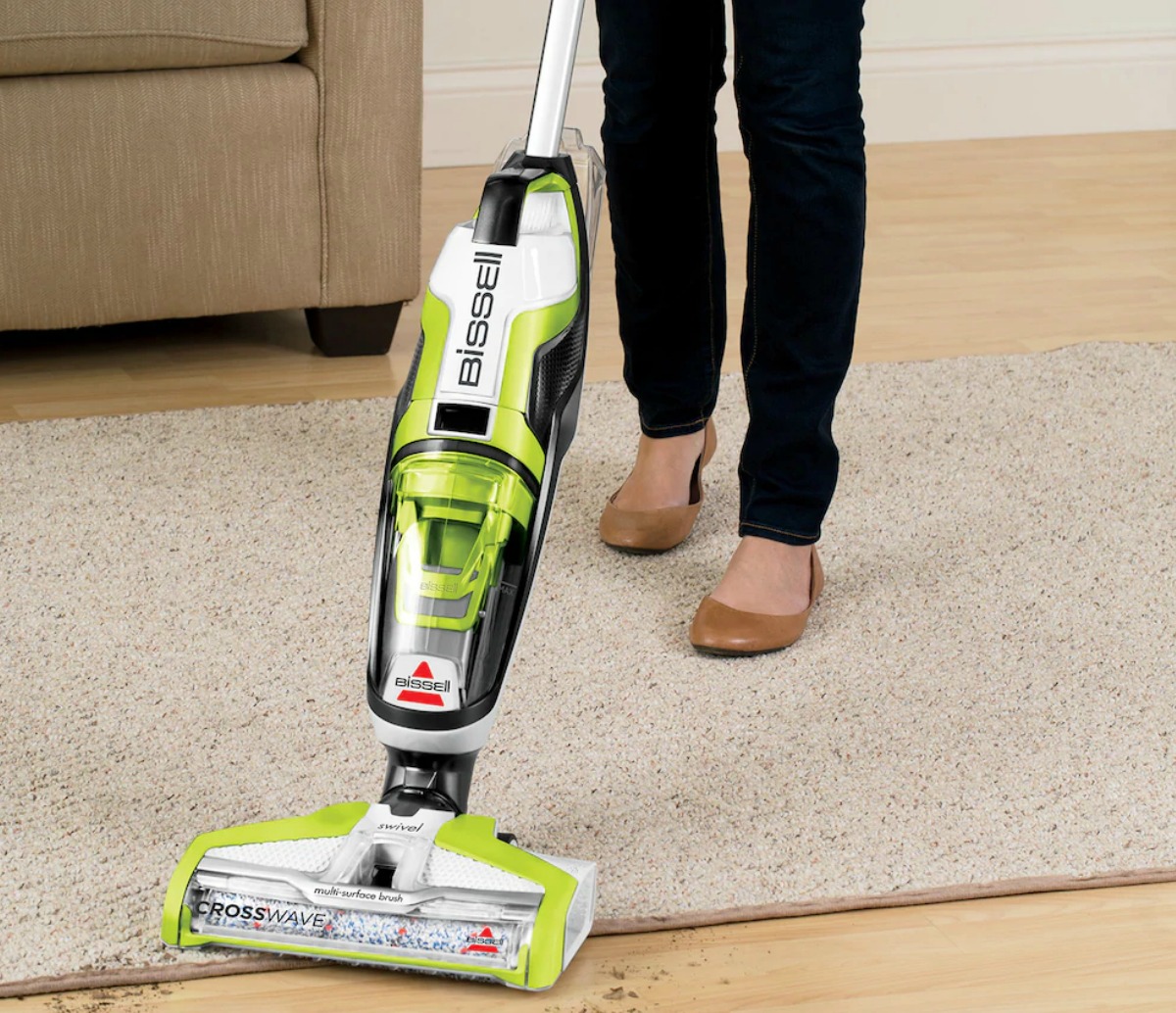 Woman using a green and white all-in-one vacuum cleaner on hardwood floors