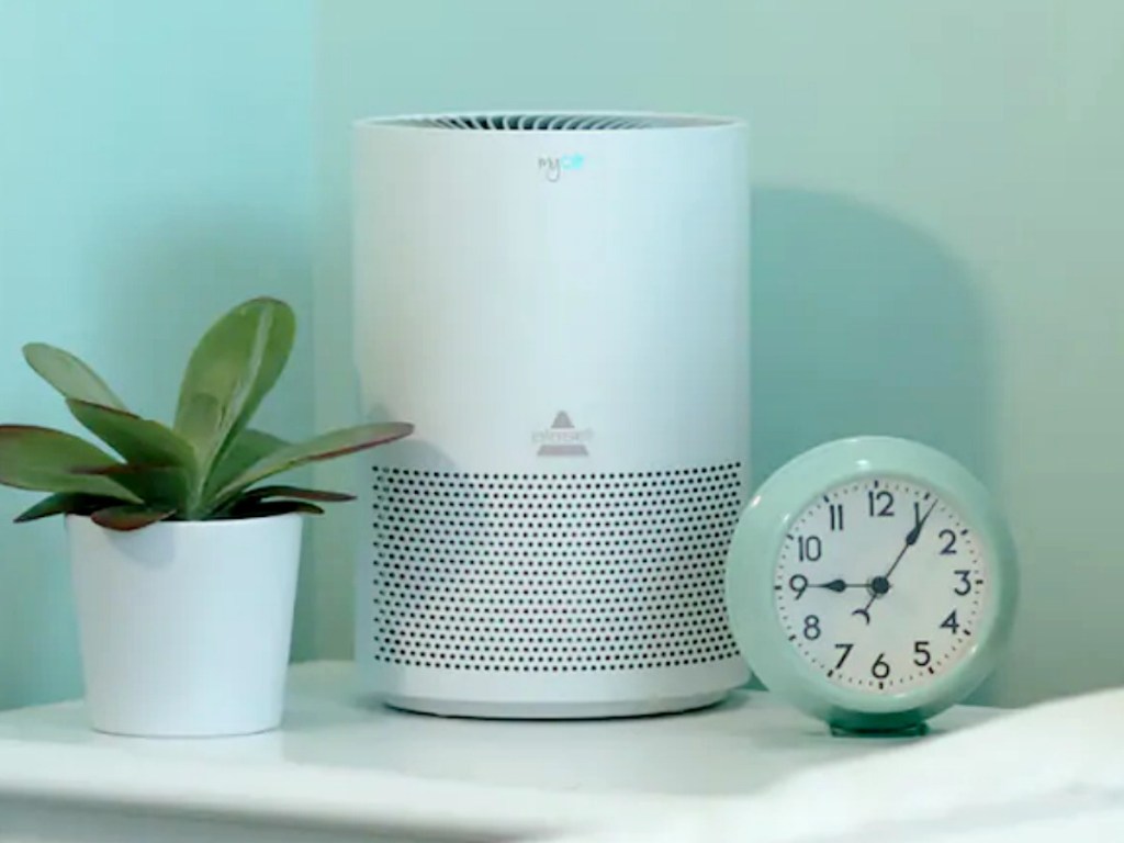 Personal sized air purifier on an end table near a plant and alarm clock