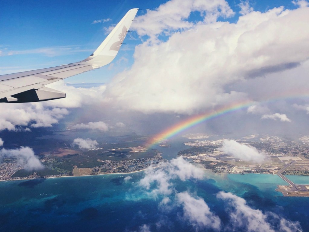 View of plane wing and clouds near rainbow over ocean