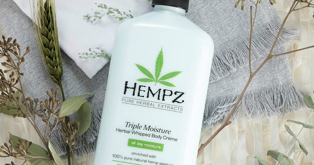 Hempz Triple Moisture Lotion laying on blanket with flowers around it