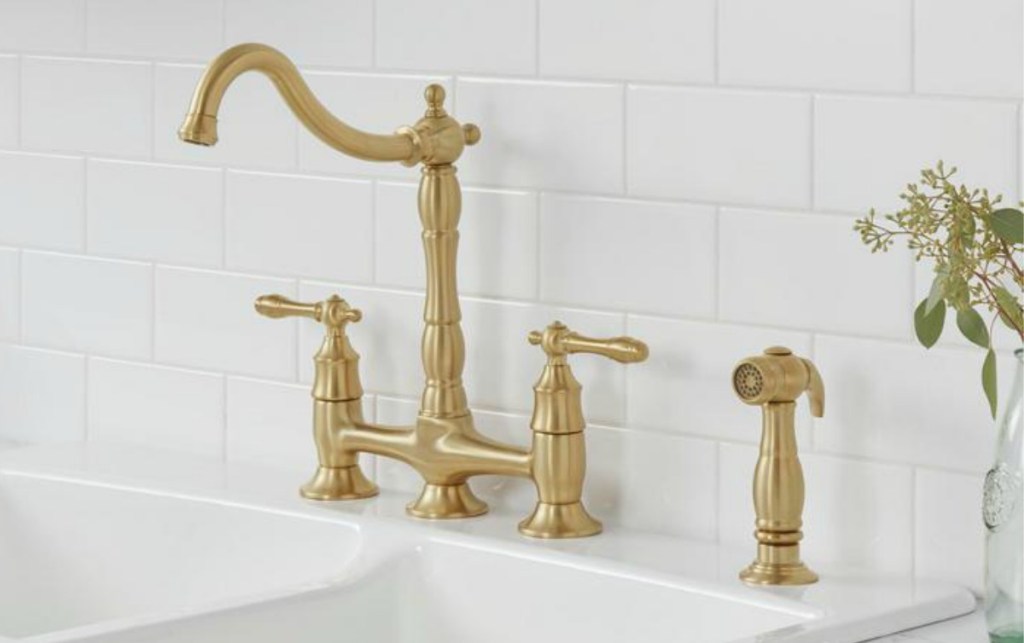 Large golden faucet with matching sprayer on sink near subway tile back-splash