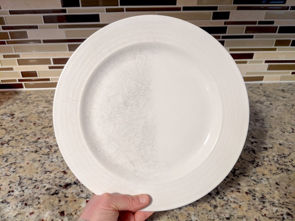 hand holding a white plate with clean side and scratched side