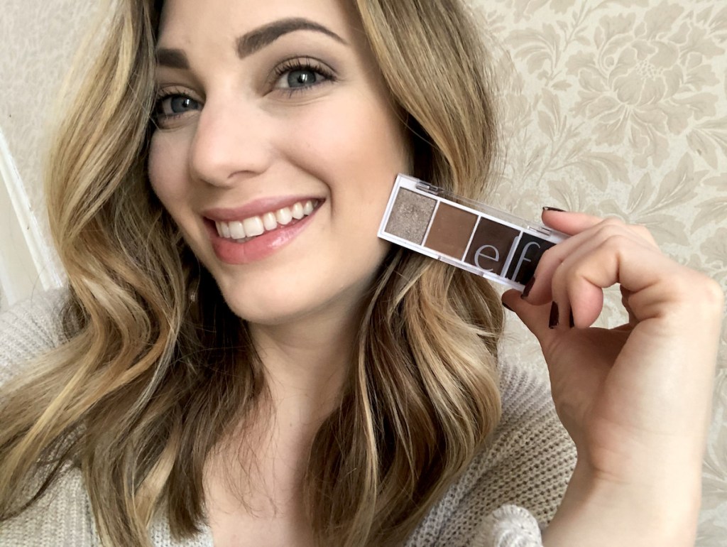 woman smiling holding small eyeshadow pallet with four colors