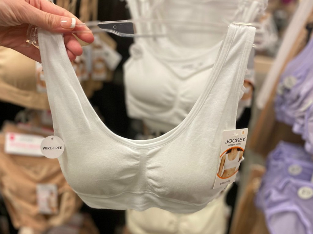 Woman holding up a woman's bra in white on hanger in front of intimates display