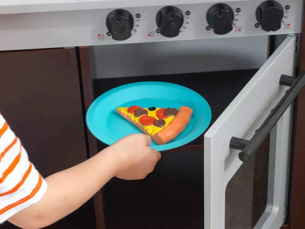 Small child putting toy food plate into kidkraft kitchen