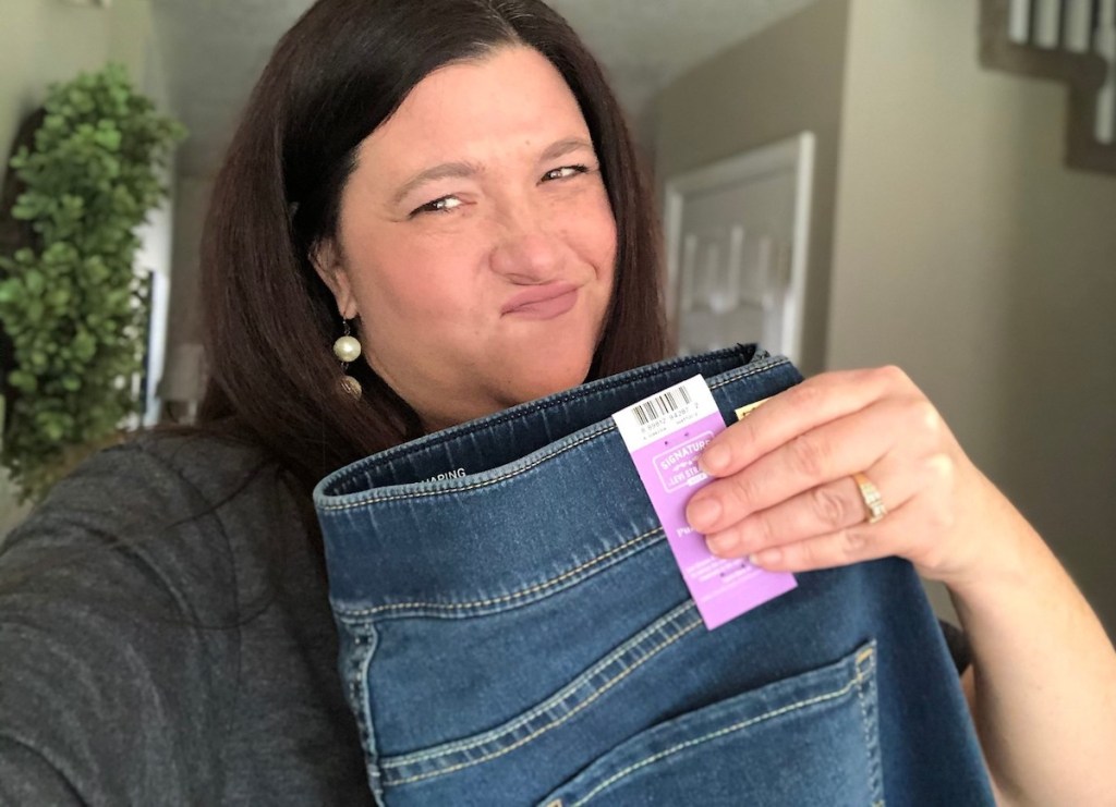 woman smirking holding a pair of jeans with tag on it 