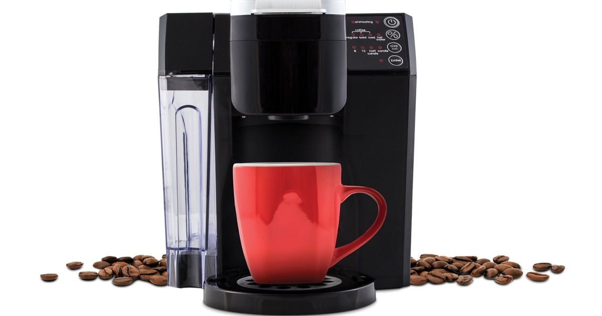 Single Brew Coffee Maker with a red mug sitting and ready for brewed coffee. There are coffee beans scattered around the coffee maker