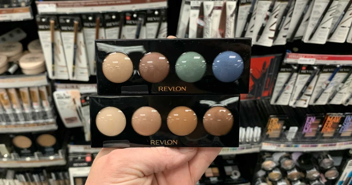Hand holding eyeshadow in front of shelf 