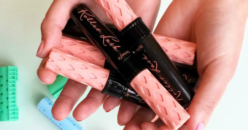 Woman holding a bunch of tubes of mascara with black bases and pink caps