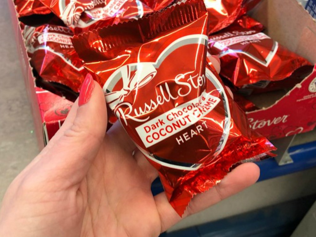Hand holding a single package of a chocolate heart near display box in store