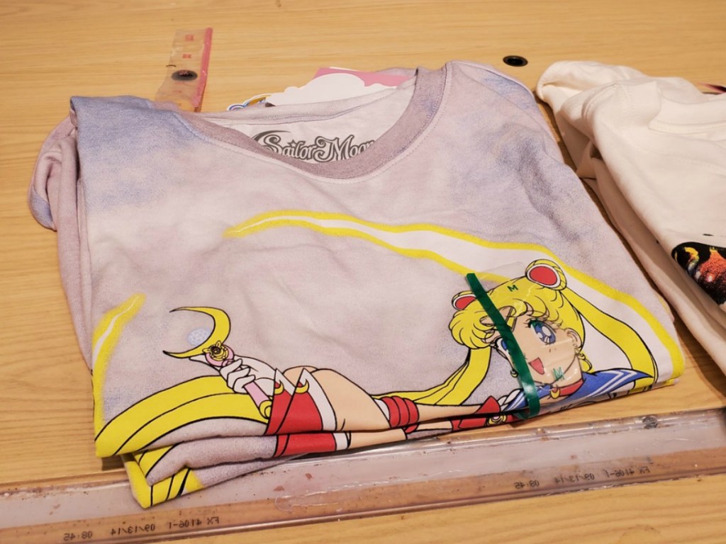 Women's graphic tee with cartoon Sailor Moon character on front, folded on wooden shelf in-store