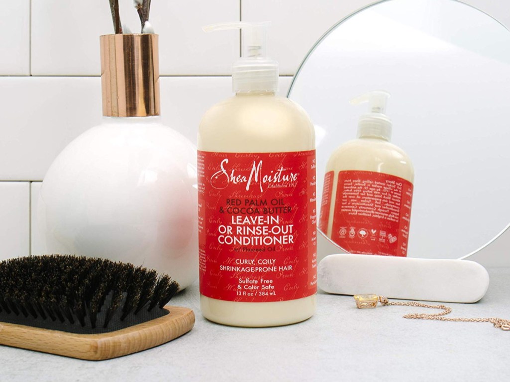 SheaMoisture conditioner on counter next to brush, mirror and necklace