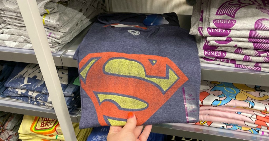 Woman's hand grabbing a folded Superman themed graphic tee shirt from store shelf