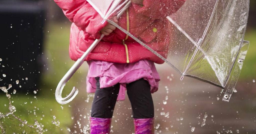 little girl with a bubble umbrella in the rain and a pink coat and boots