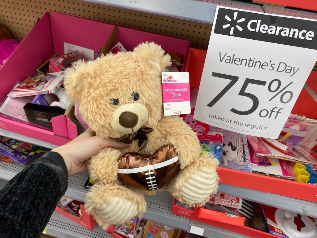 hand holding a plush bear by a sign at Walmart
