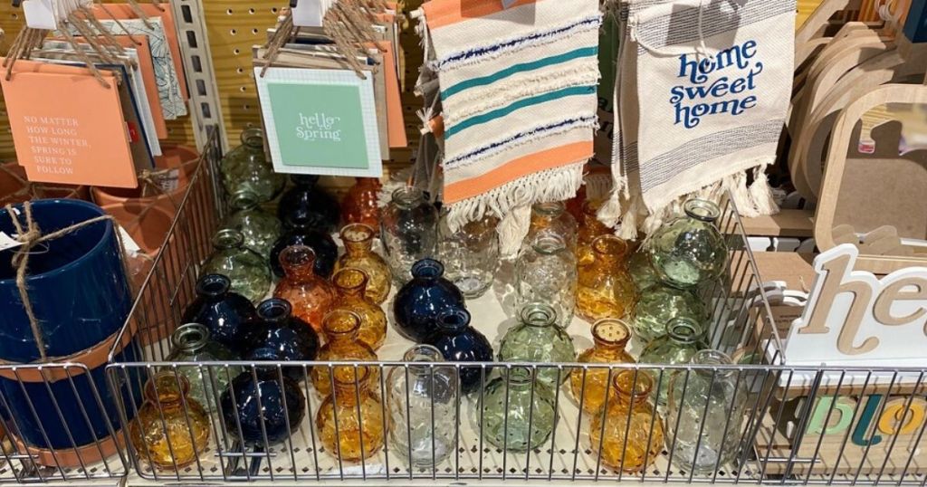 store shelf with small glass bud vases, decorative signs, and dishtowels