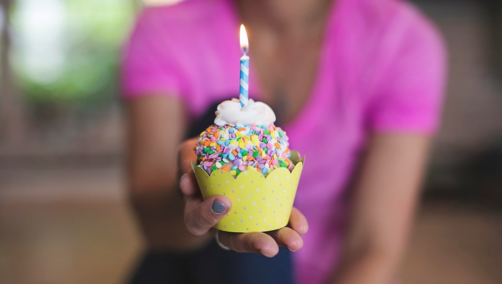 person holding confetti cupcake with candle in middle