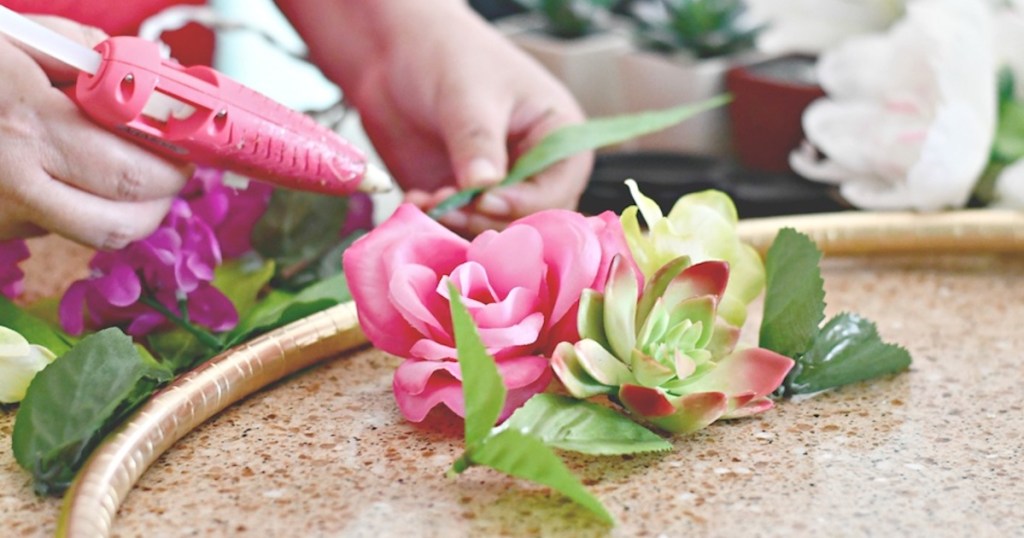 hands using hot glue gun to place colorful florals on gold hula hoop - dollar tree wedding