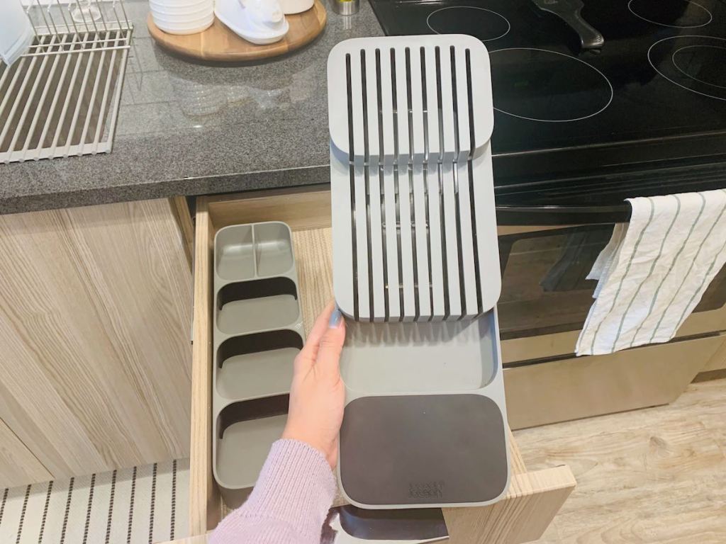 hand holding a gray knife drawer organizer in kitchen